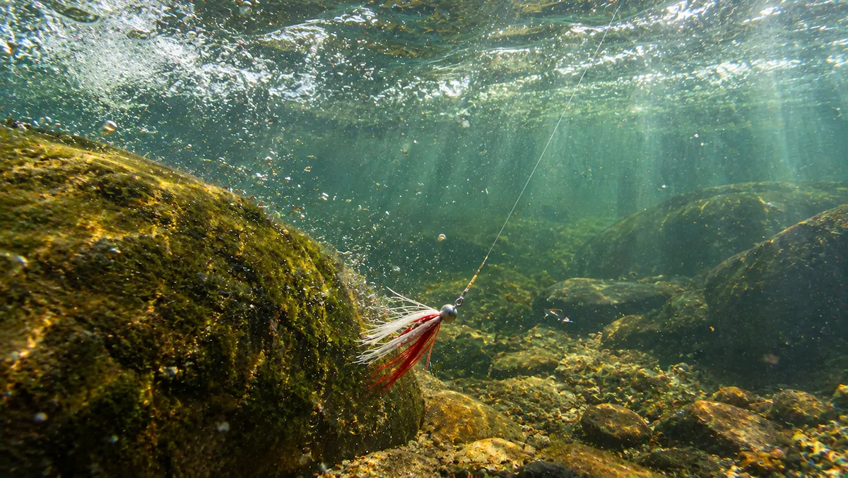 Isca jig com saia de pelo descendo até o fundo de um poço de rio com correnteza